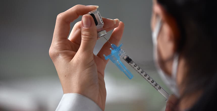 Profissional de saúde prepara dose de vacina com seringa e frasco